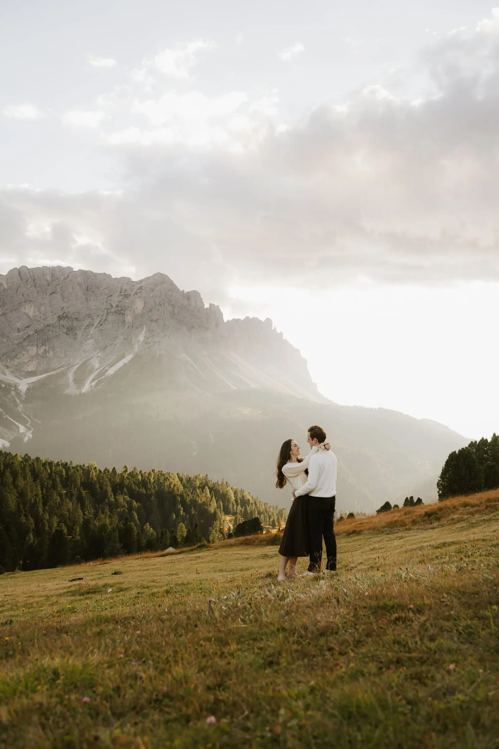 Couple embracing in the meadow as the sun sets over Passo delle Erbe