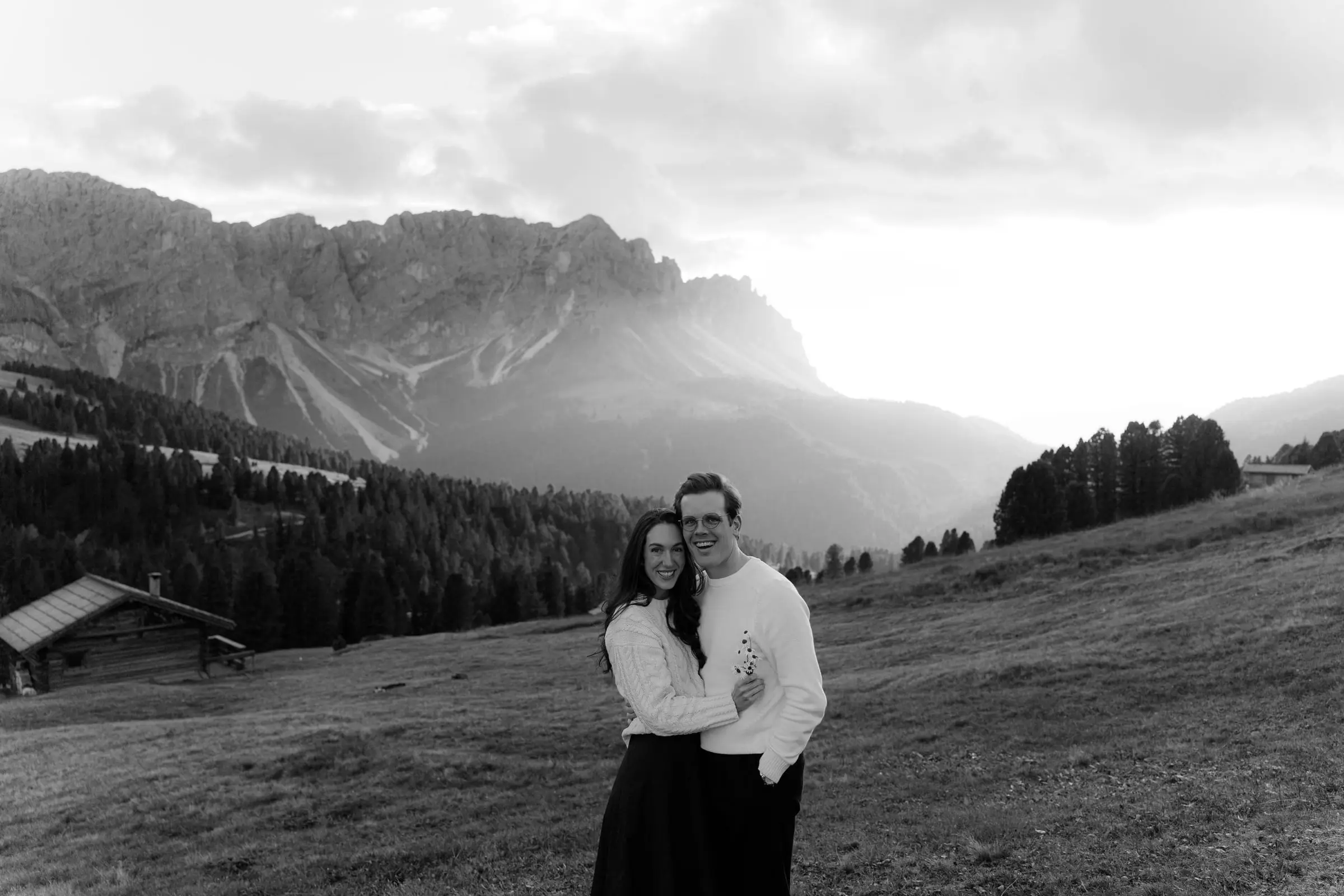 Black and white photo of the couple embracing in the meadow at sunset