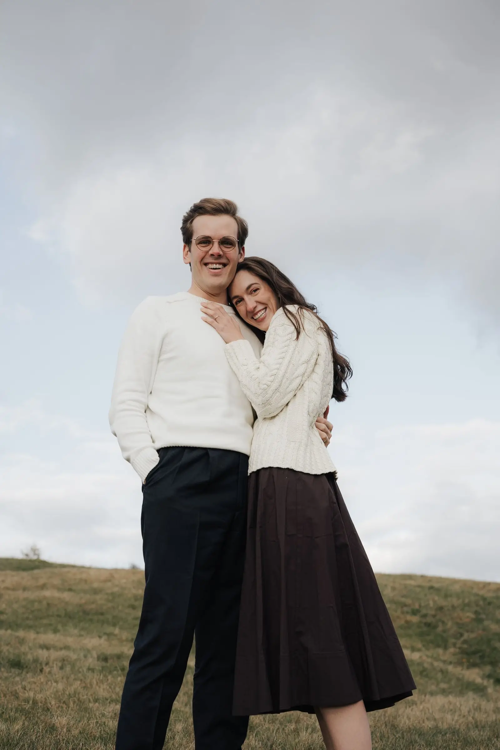 Laughing couple hugging under a cloudy sky