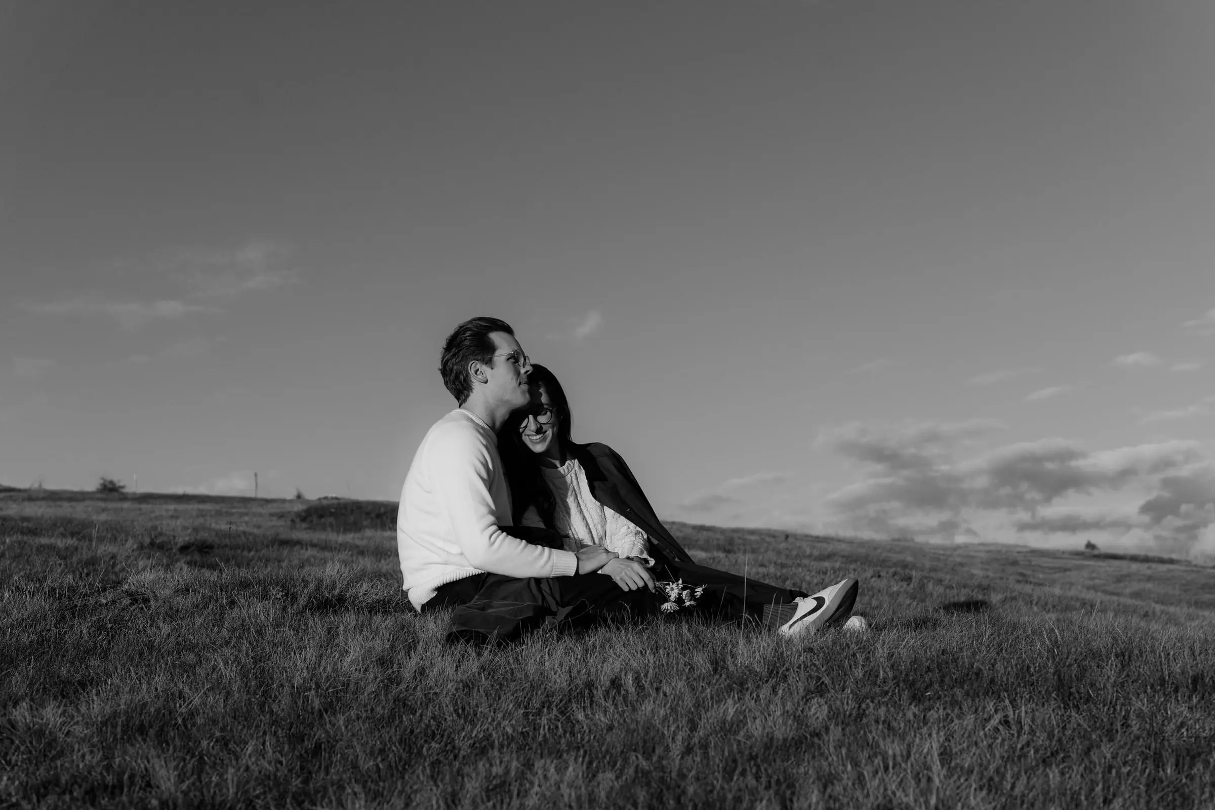 Black and white photo of the couple sitting close in the grass