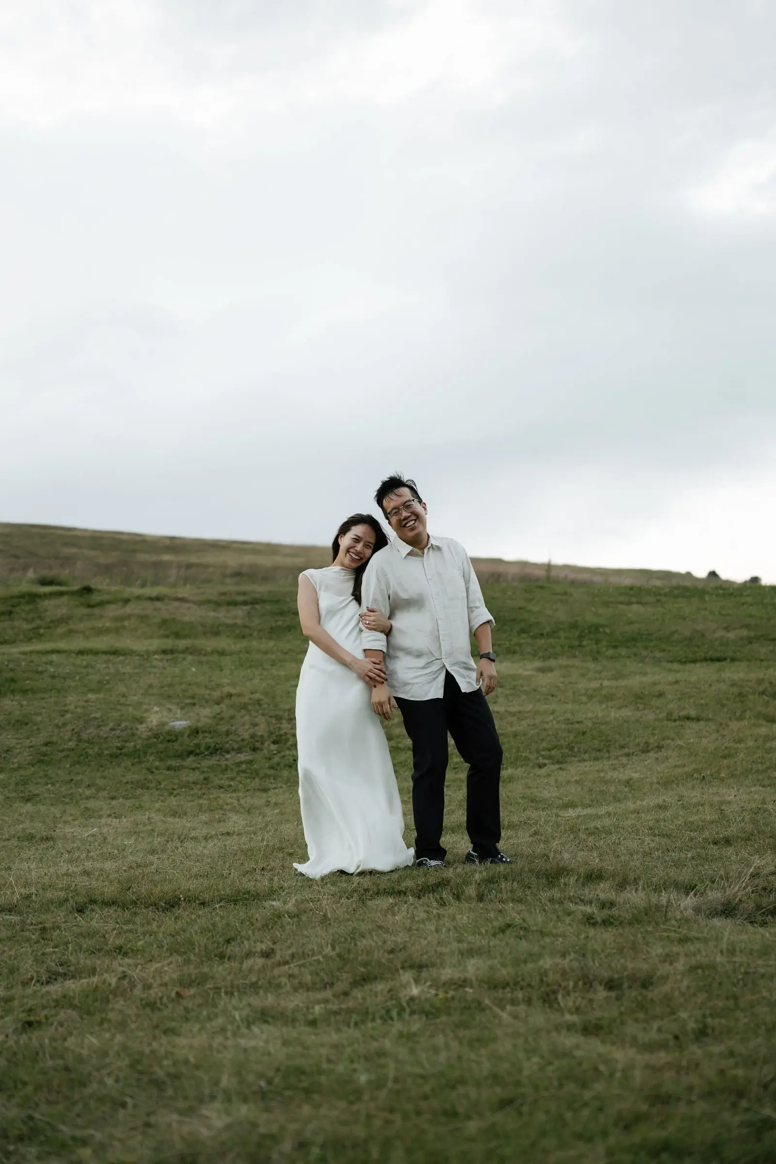Couple in white standing close in the meadow under a grey sky
