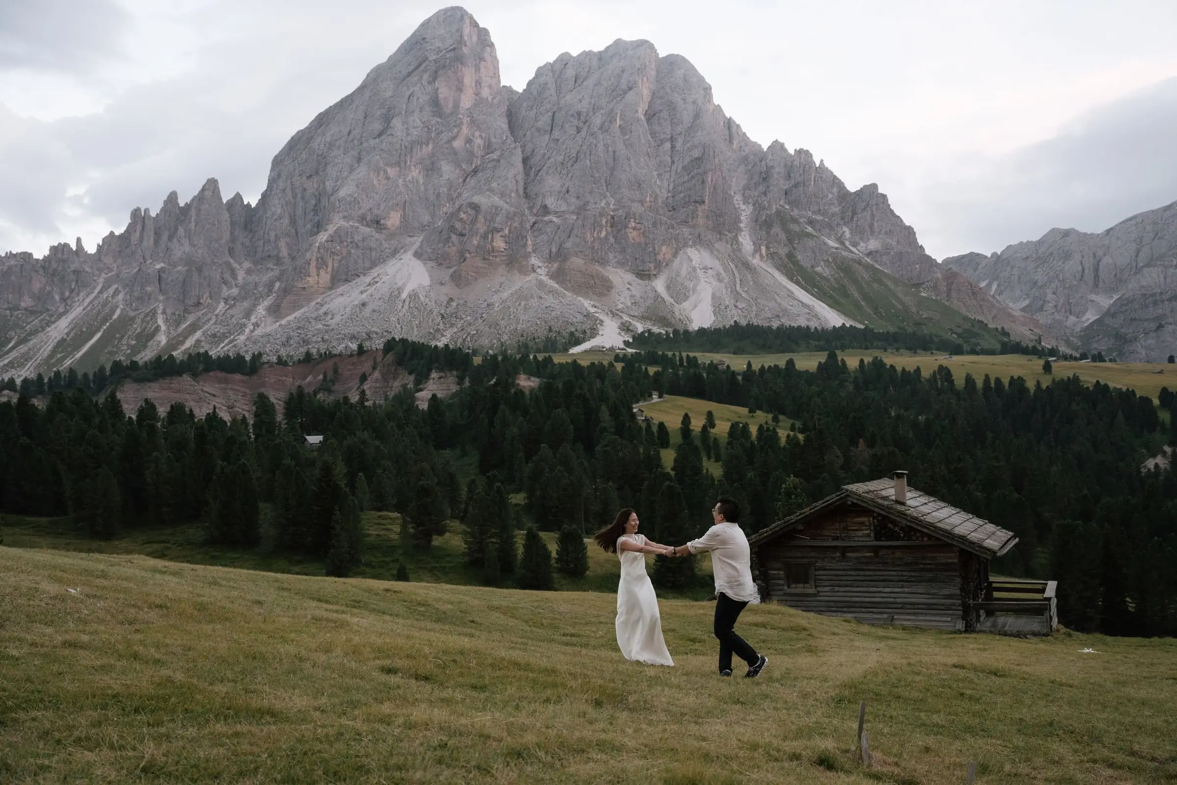 Couple dancing in front of a wooden hut below the Sass de Putia