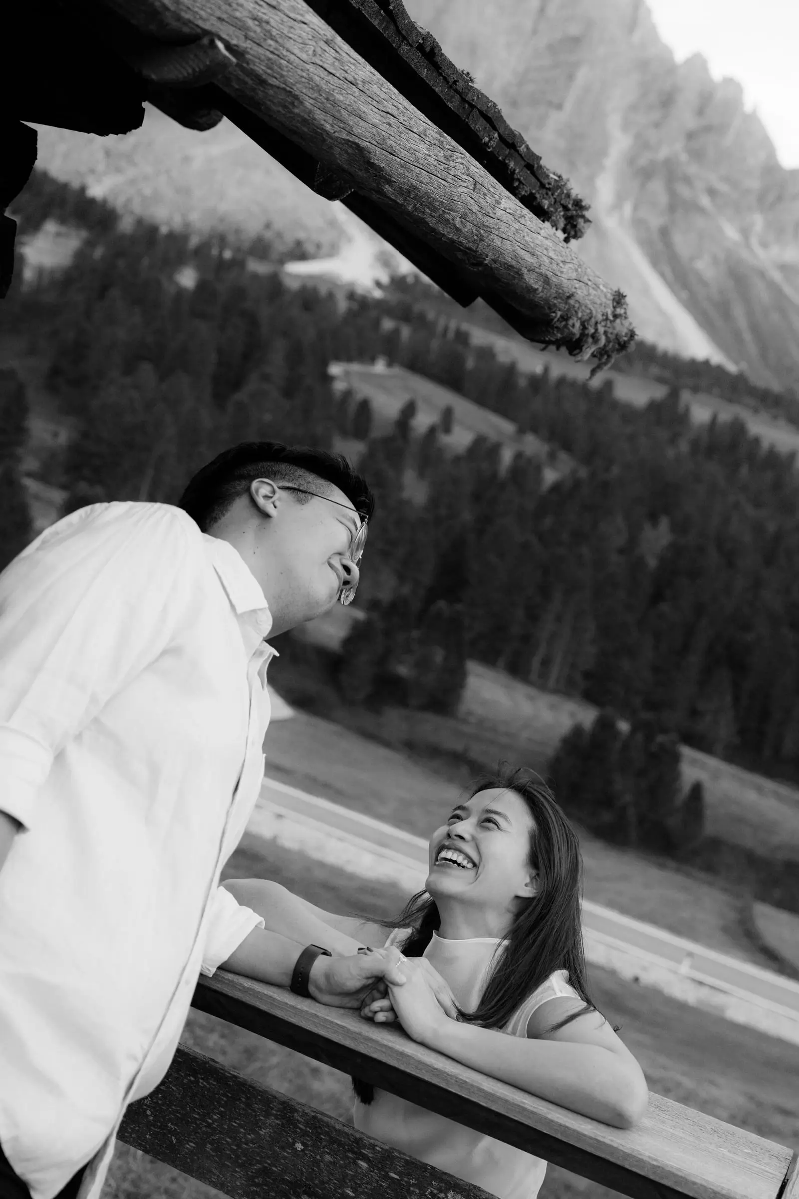 Black and white photo of the couple laughing at the wooden railing of a hut