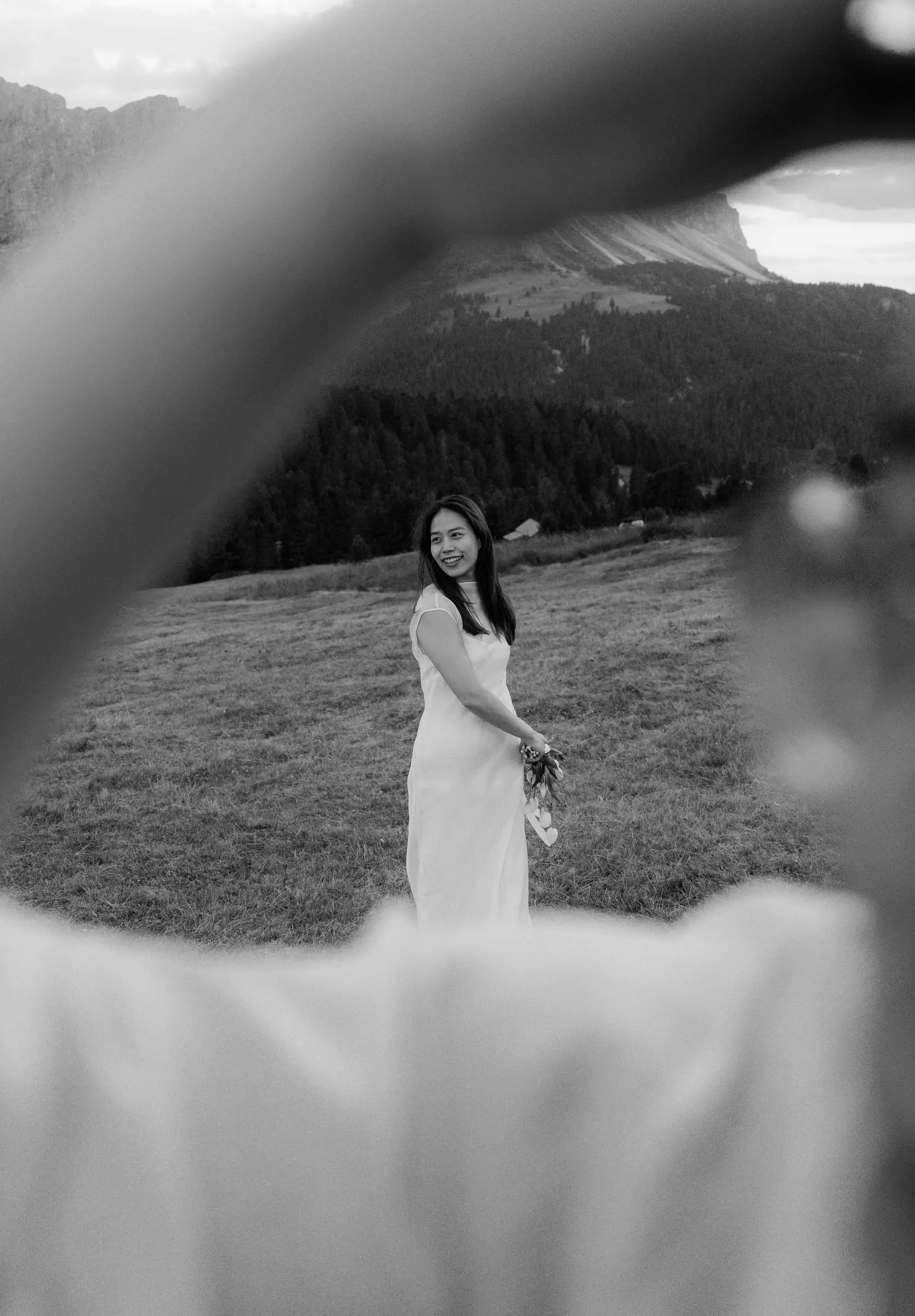 Black and white photo of her smiling in the meadow, framed by his arm