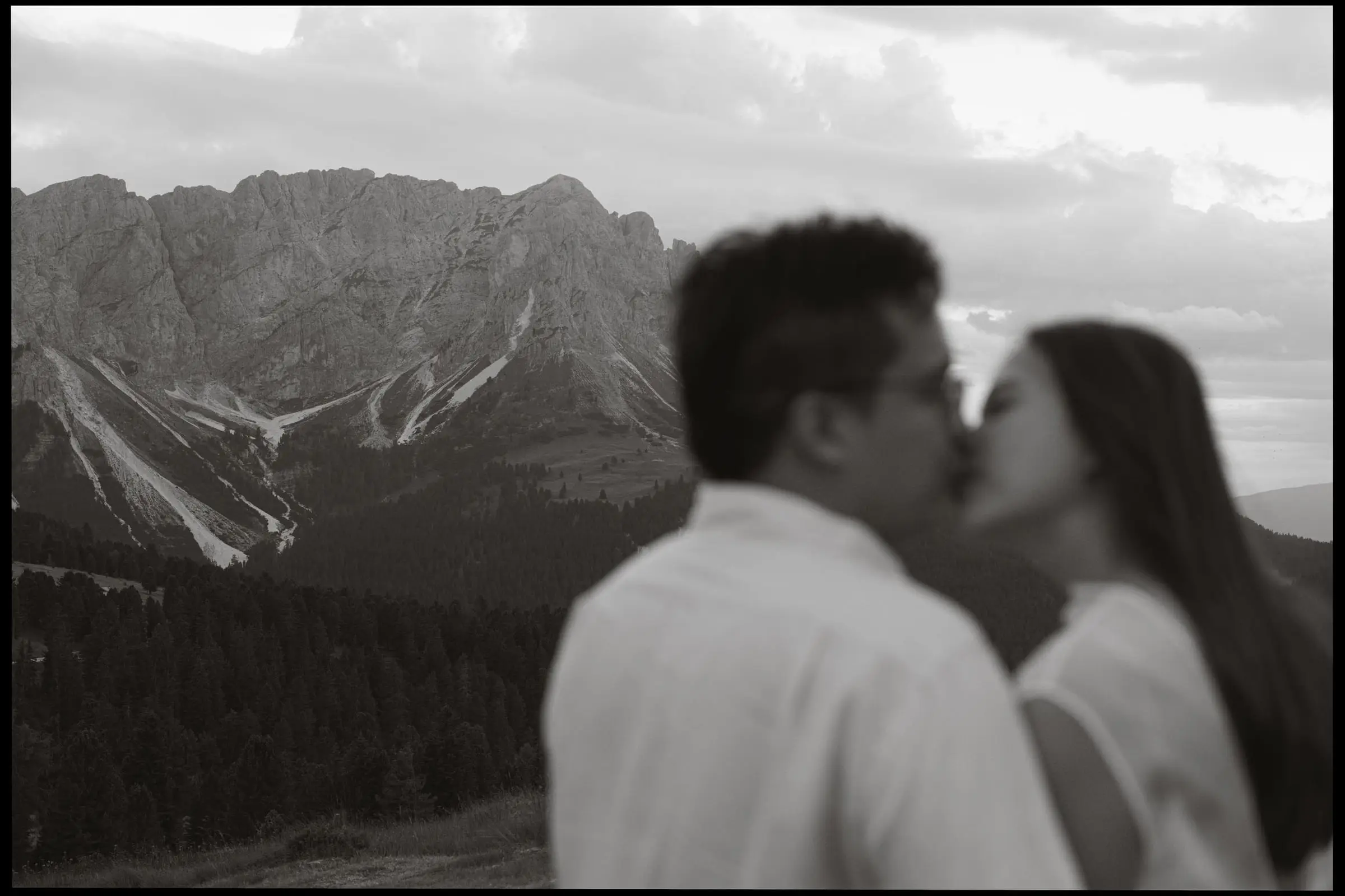 Black and white photo of the couple kissing with mountains behind, on film