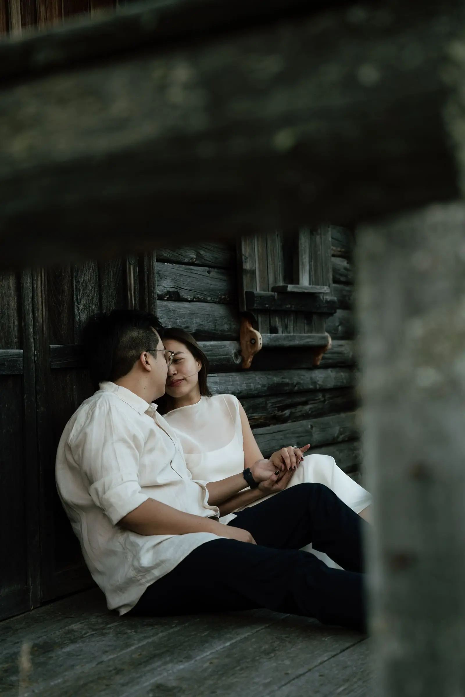 Couple sitting on the porch of a wooden hut, seen through the beams
