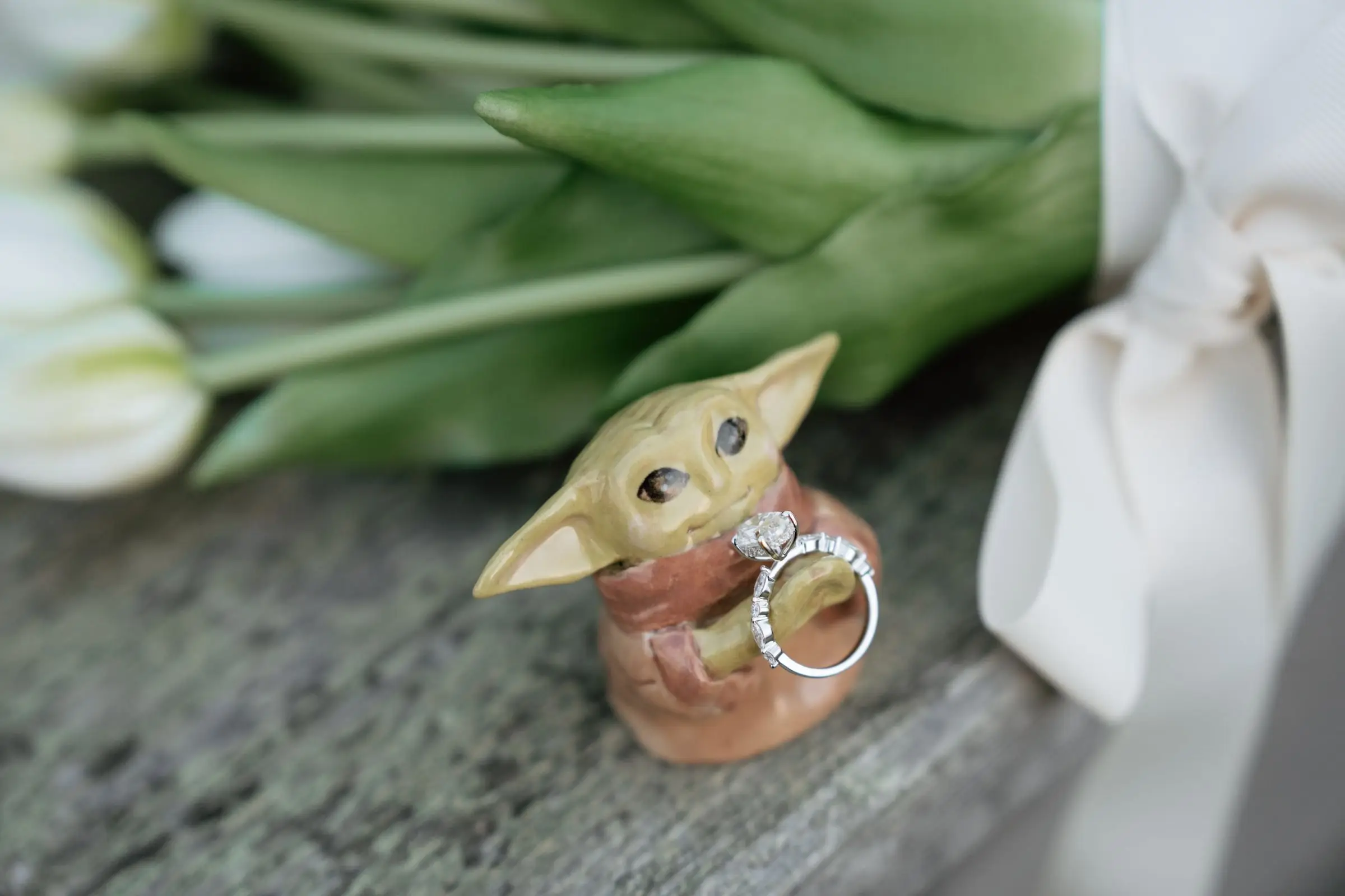 Diamond engagement ring on a small figurine beside white tulips