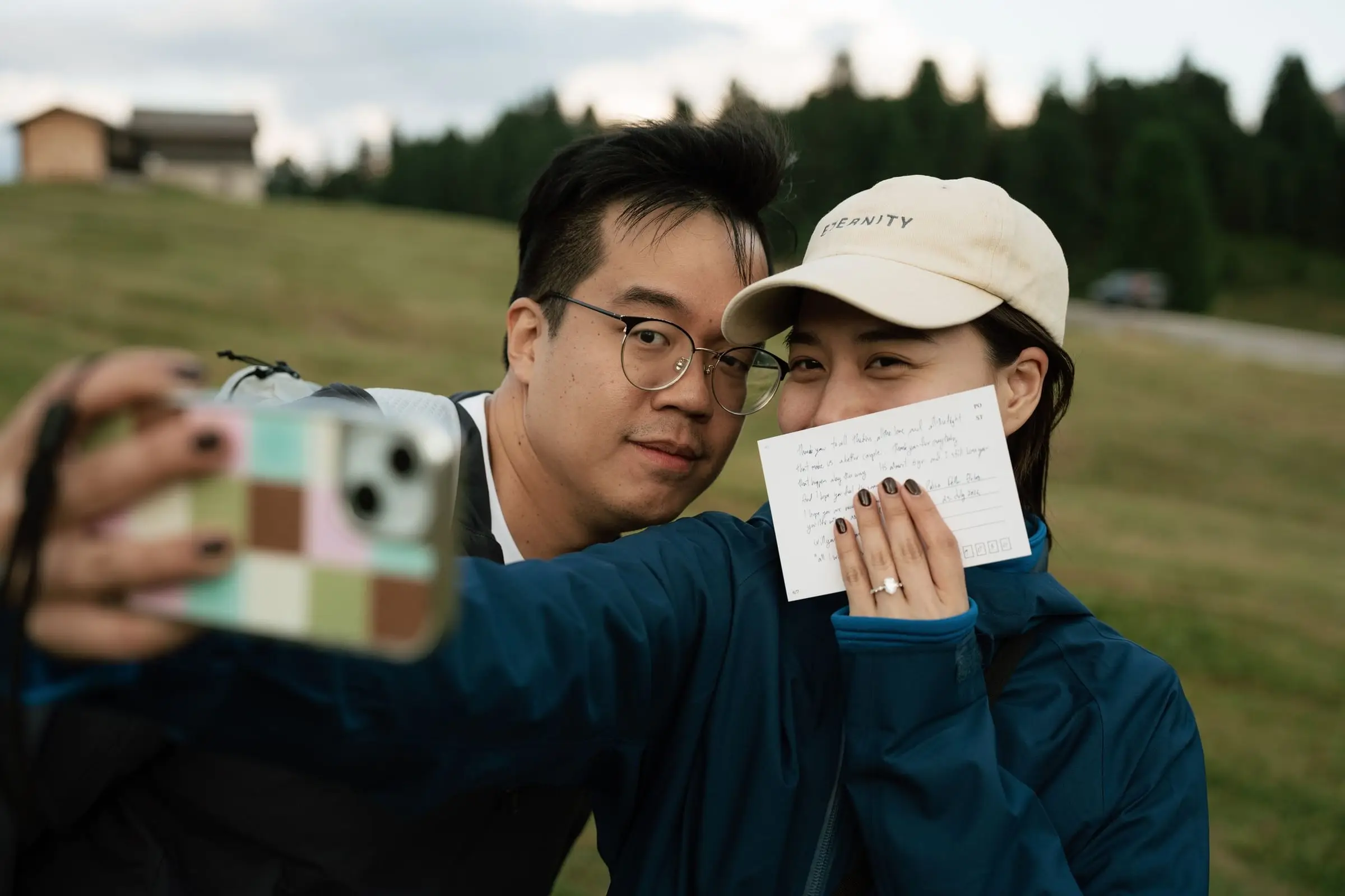 The newly engaged couple taking a selfie, she holds the letter and shows the ring