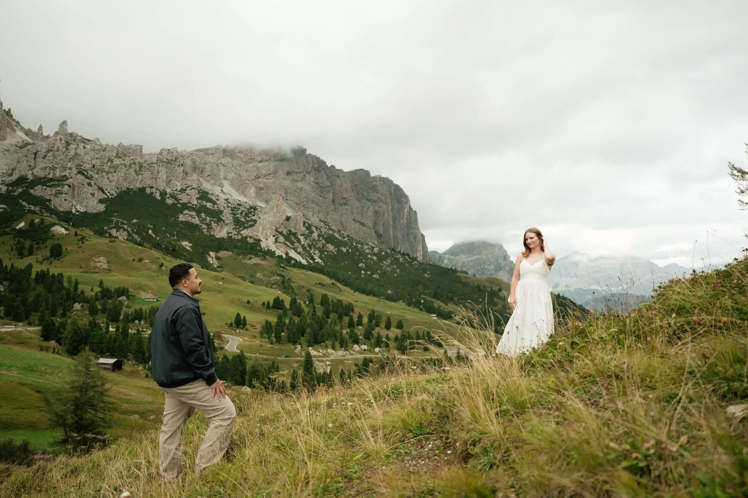 Couple on a grassy slope at Passo Gardena, clouds over the Dolomites