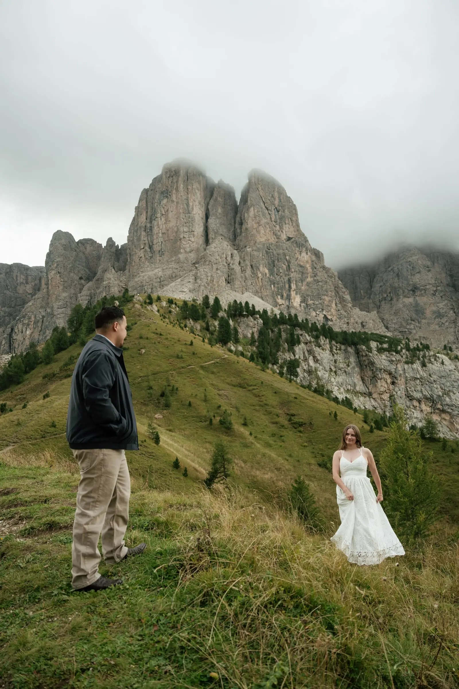 Couple on a steep meadow below the rock walls of Passo Gardena