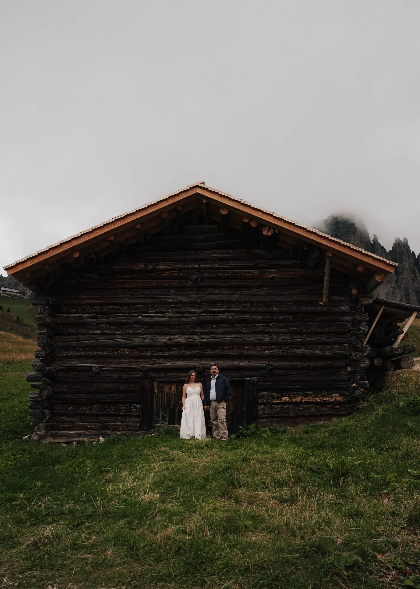 Couple standing in front of a large wooden barn in the mist