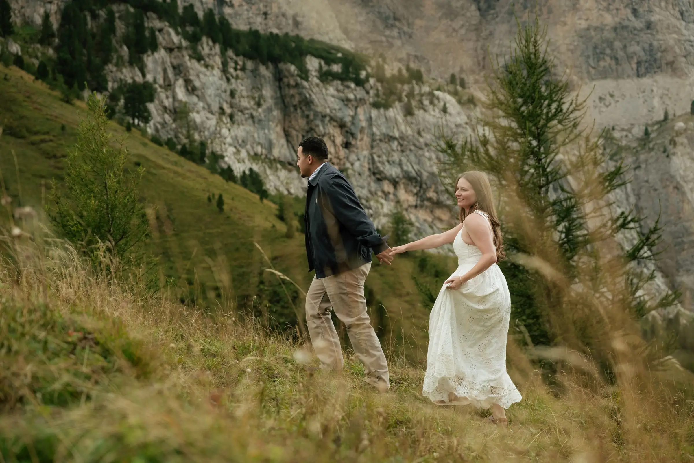 Couple walking hand in hand through golden grass below the rock walls
