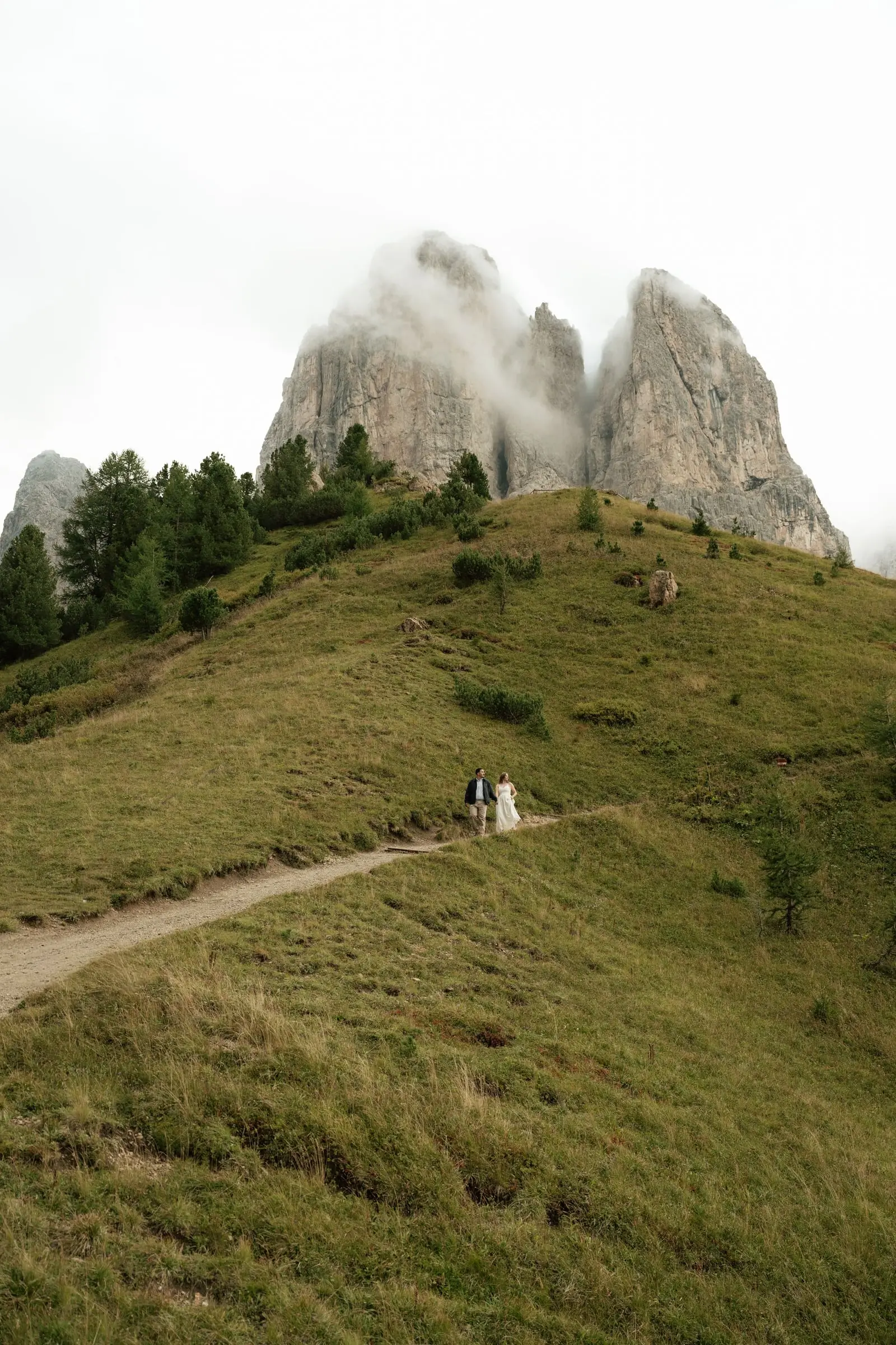 Couple small on the path below the rock towers of Passo Gardena