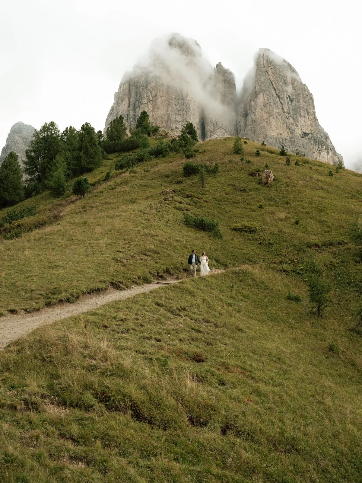 Couple small on the path below the rock towers of Passo Gardena