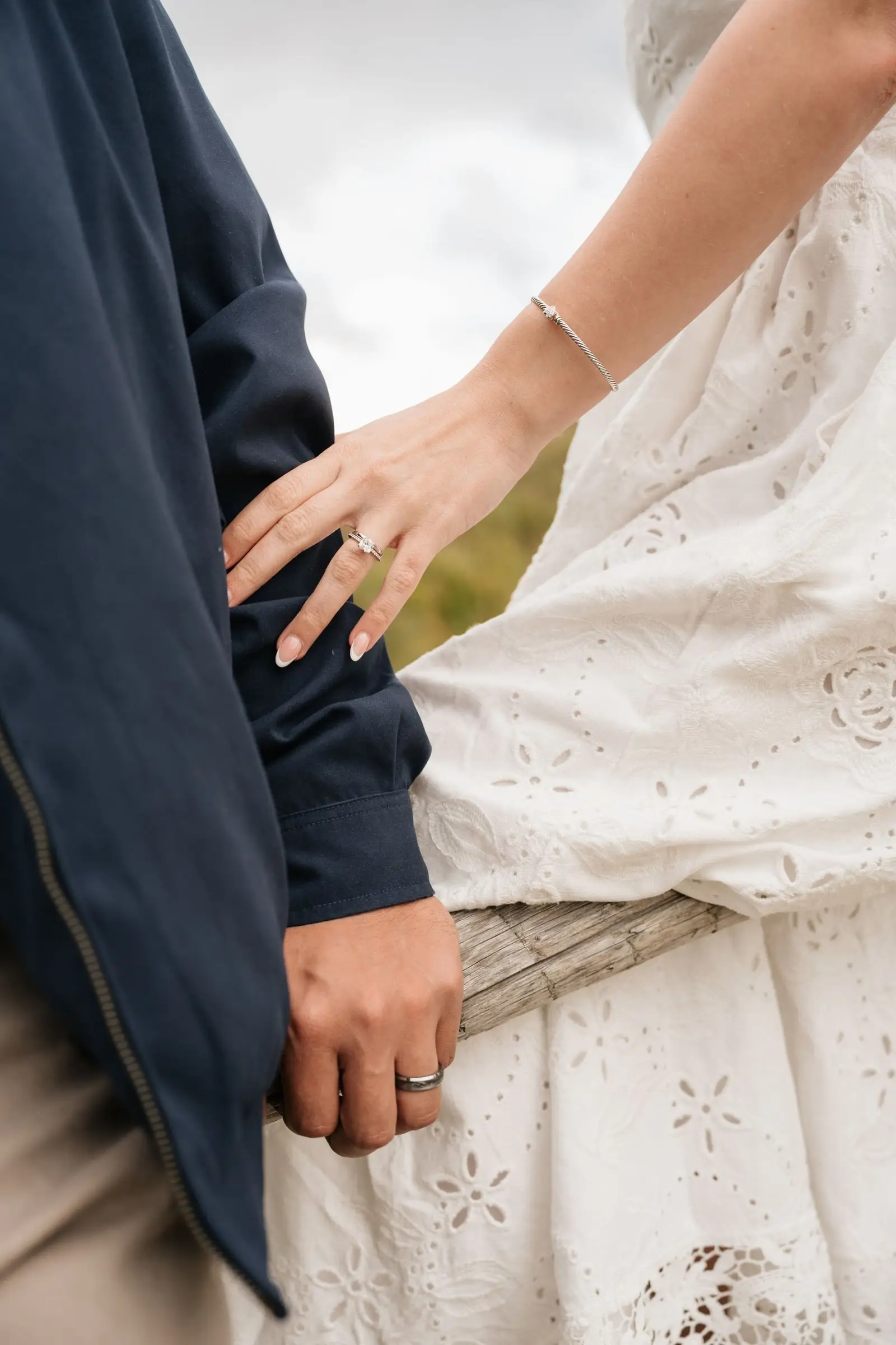 Close-up of her hand with a ring on his arm, her white eyelet dress