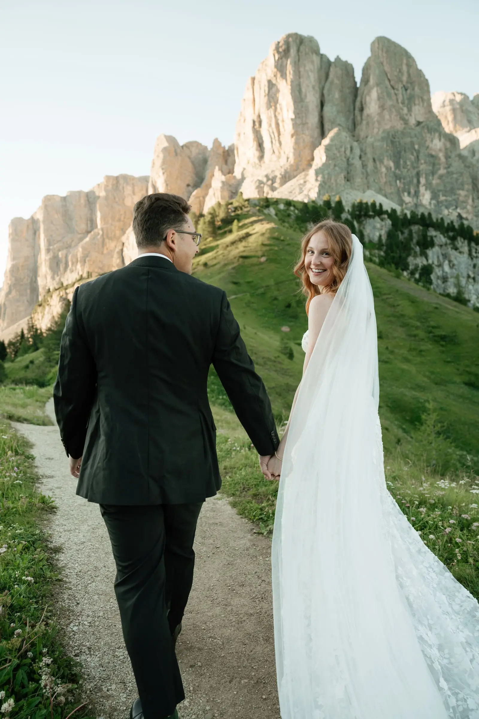 She looks back and smiles in a lace gown and long veil on the trail