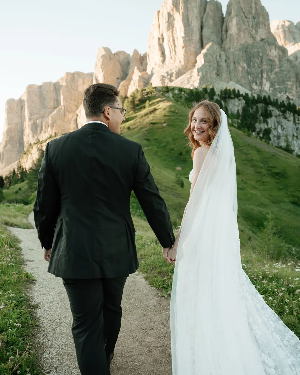 She looks back and smiles in a lace gown and long veil on the trail