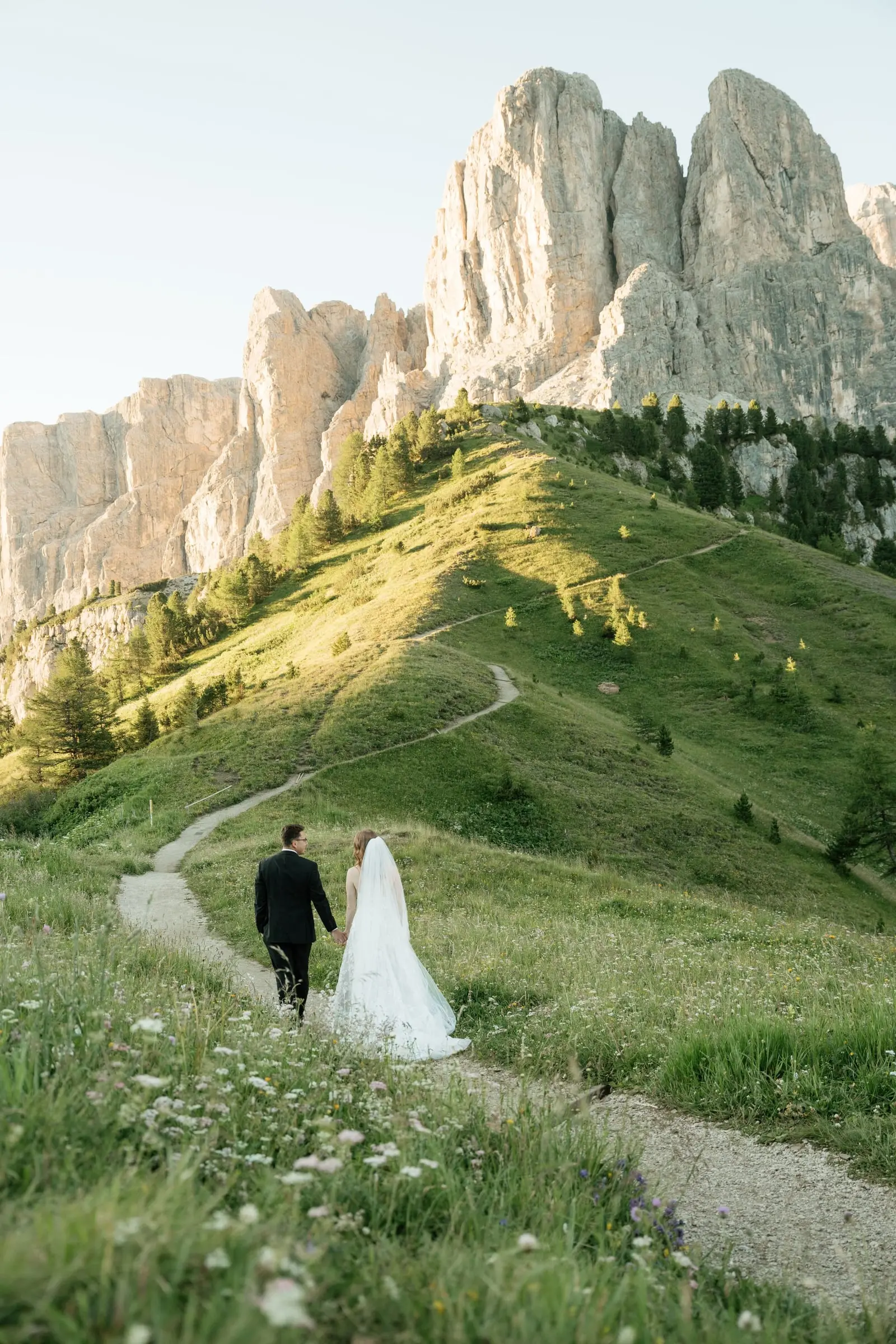 Couple walking a winding path through wildflower meadows below the Dolomites