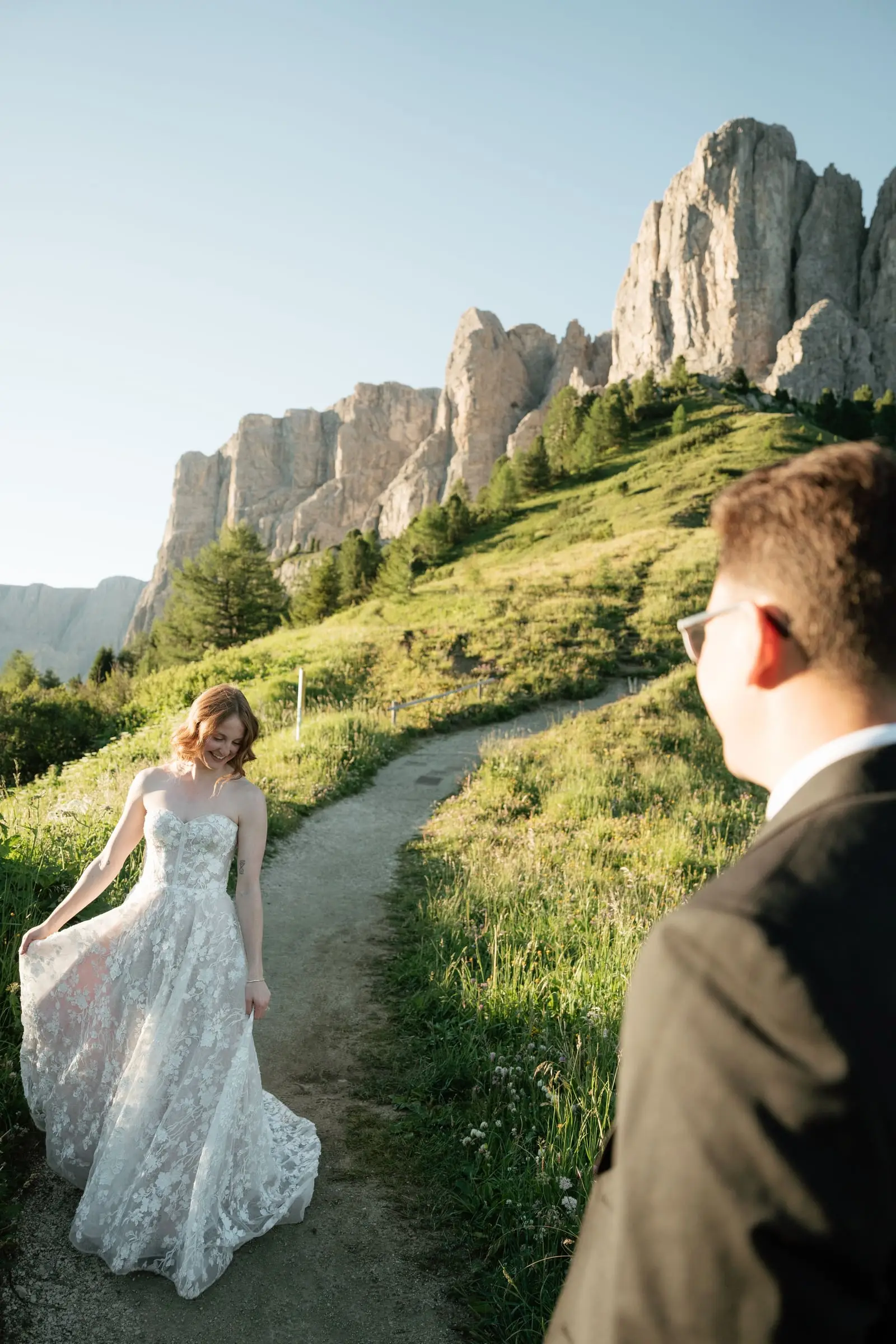 She twirls her lace gown on the path as he watches