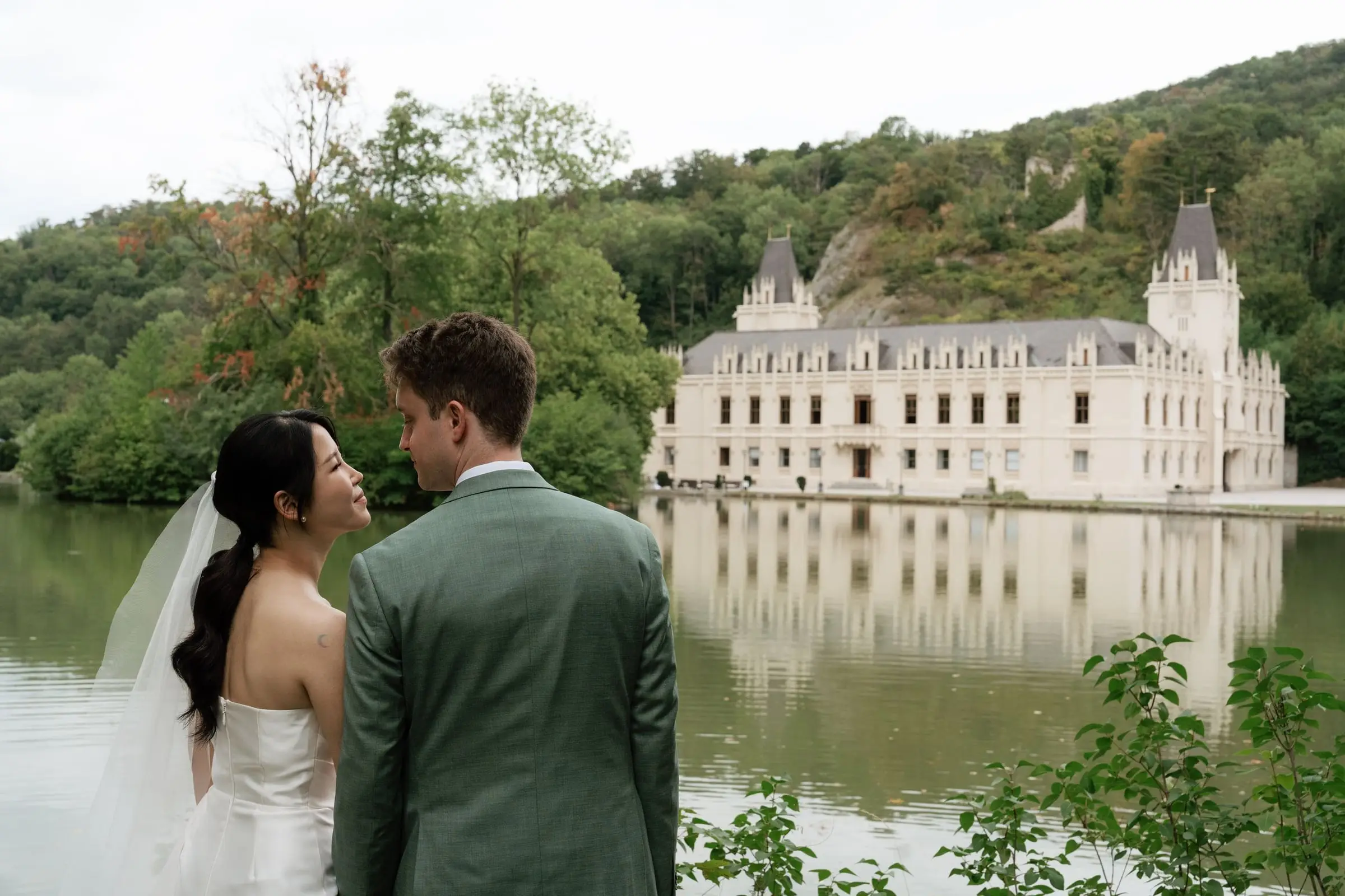 Bride and groom by the lake with Schloss Hernstein reflected in the water