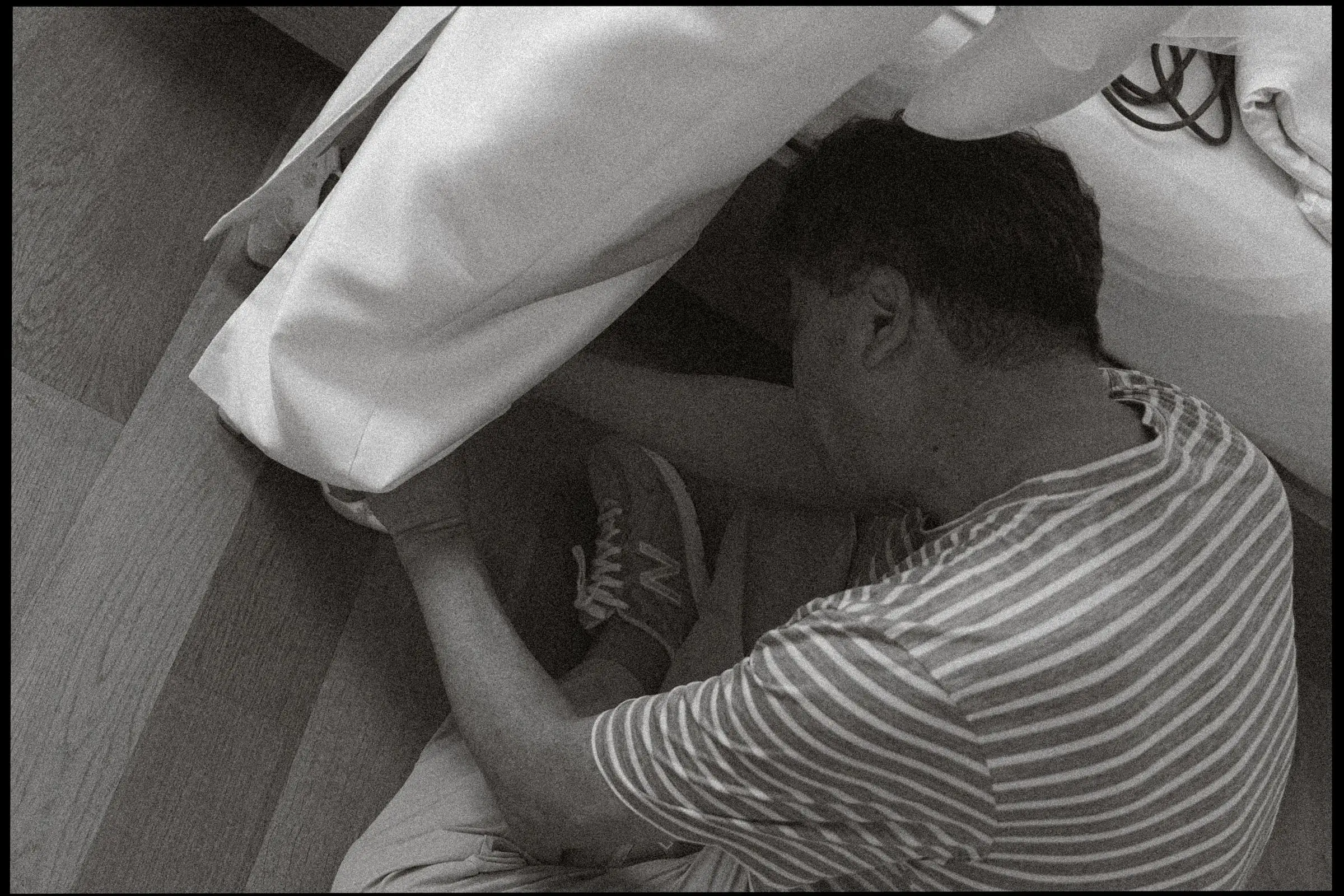Black and white photo of a guest helping with the bride's shoes, on film