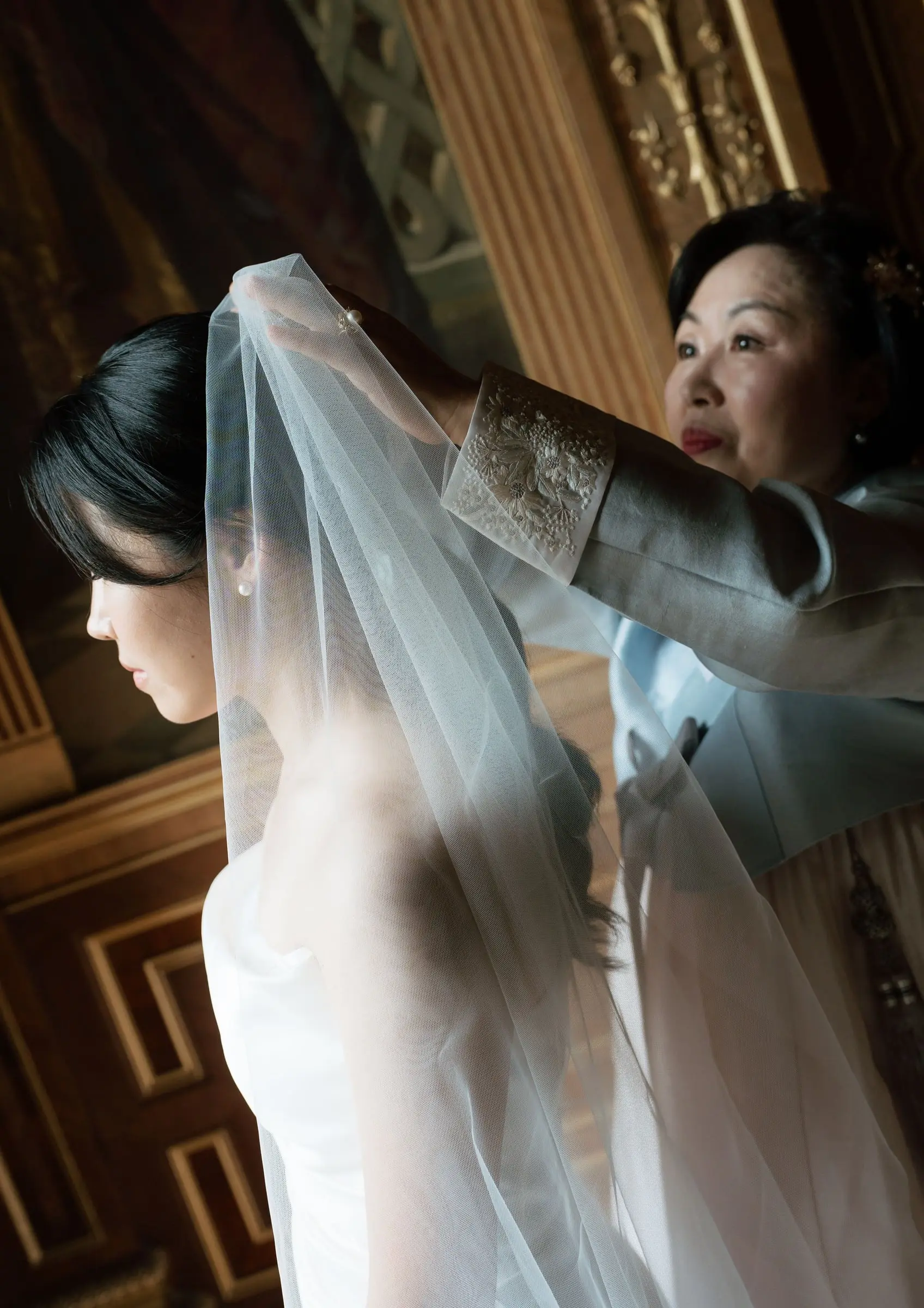 Mother adjusting the bride's veil in a golden room