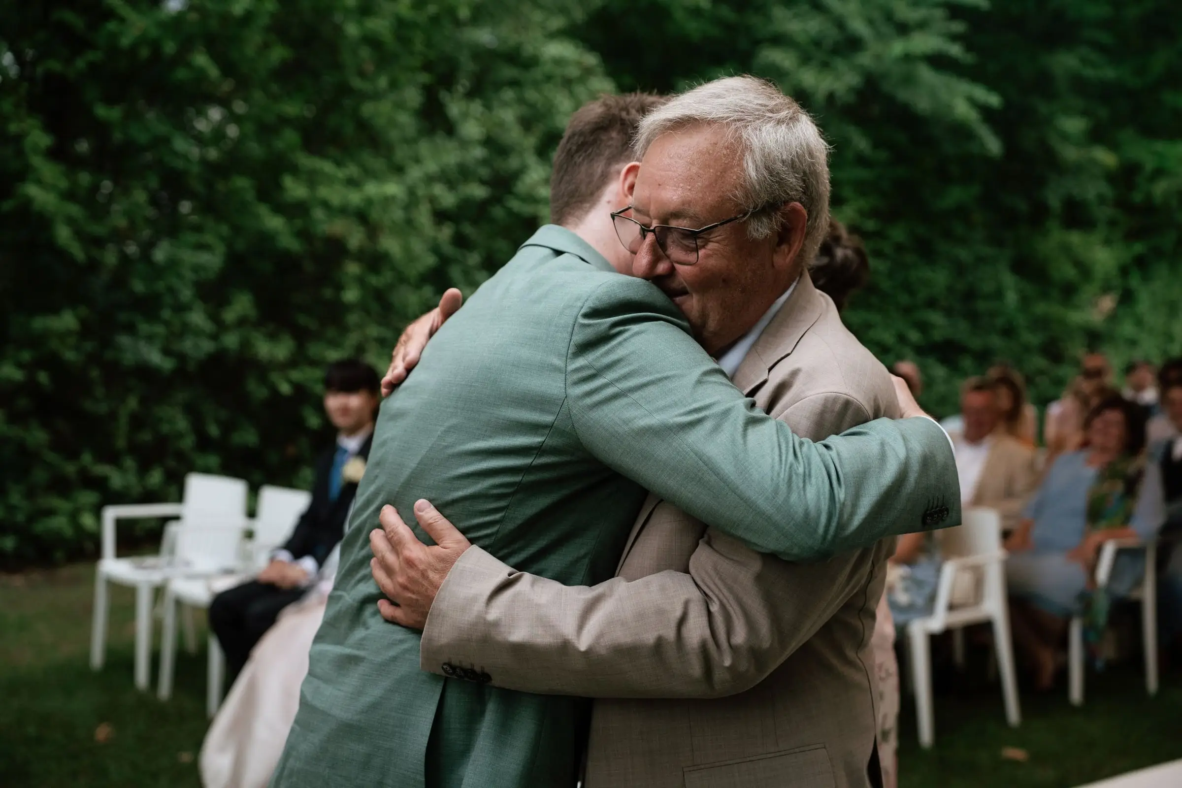 Groom in a sage suit hugging an older guest at the ceremony
