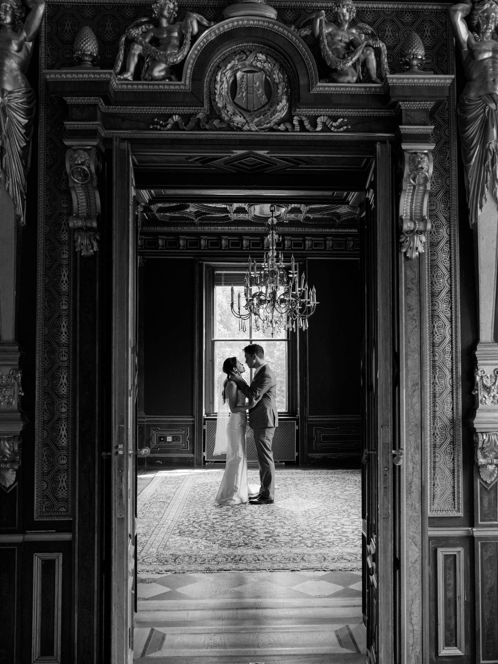 Black and white photo of the couple embracing, framed by carved castle doors