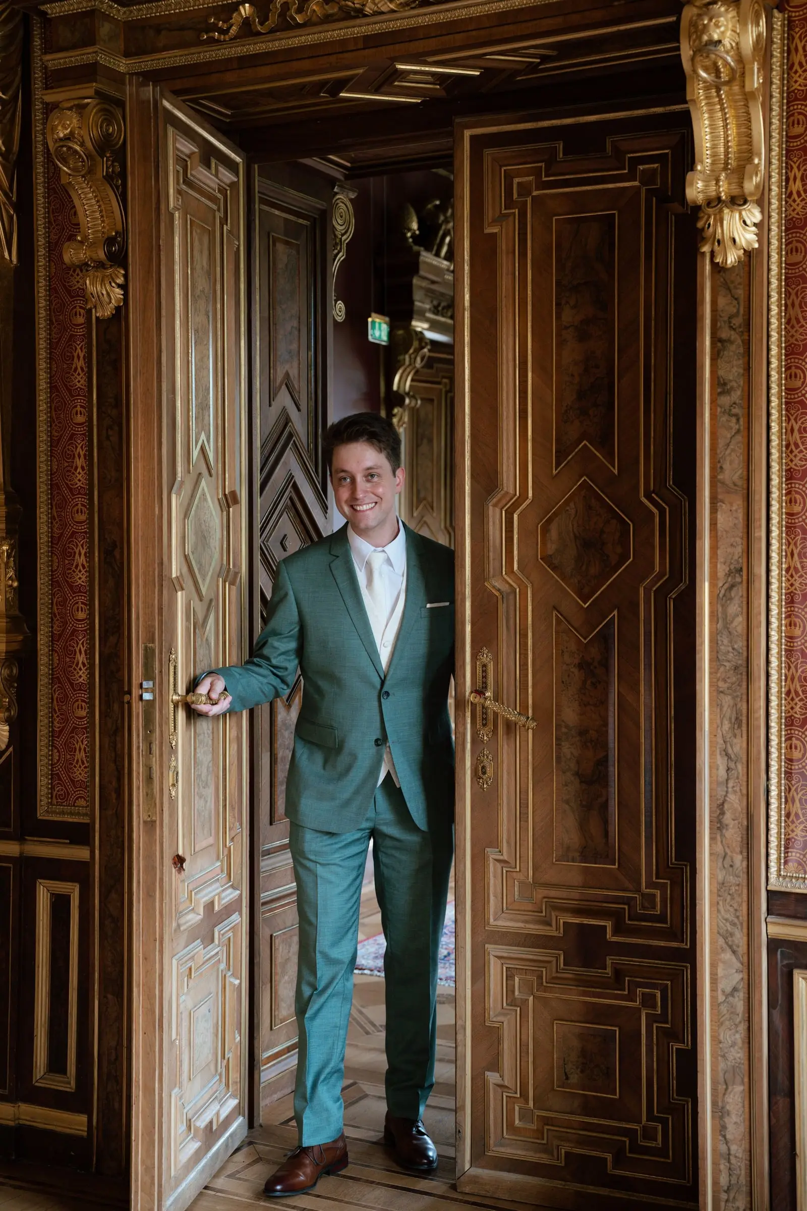 Groom opening a tall wooden door inside Schloss Hernstein