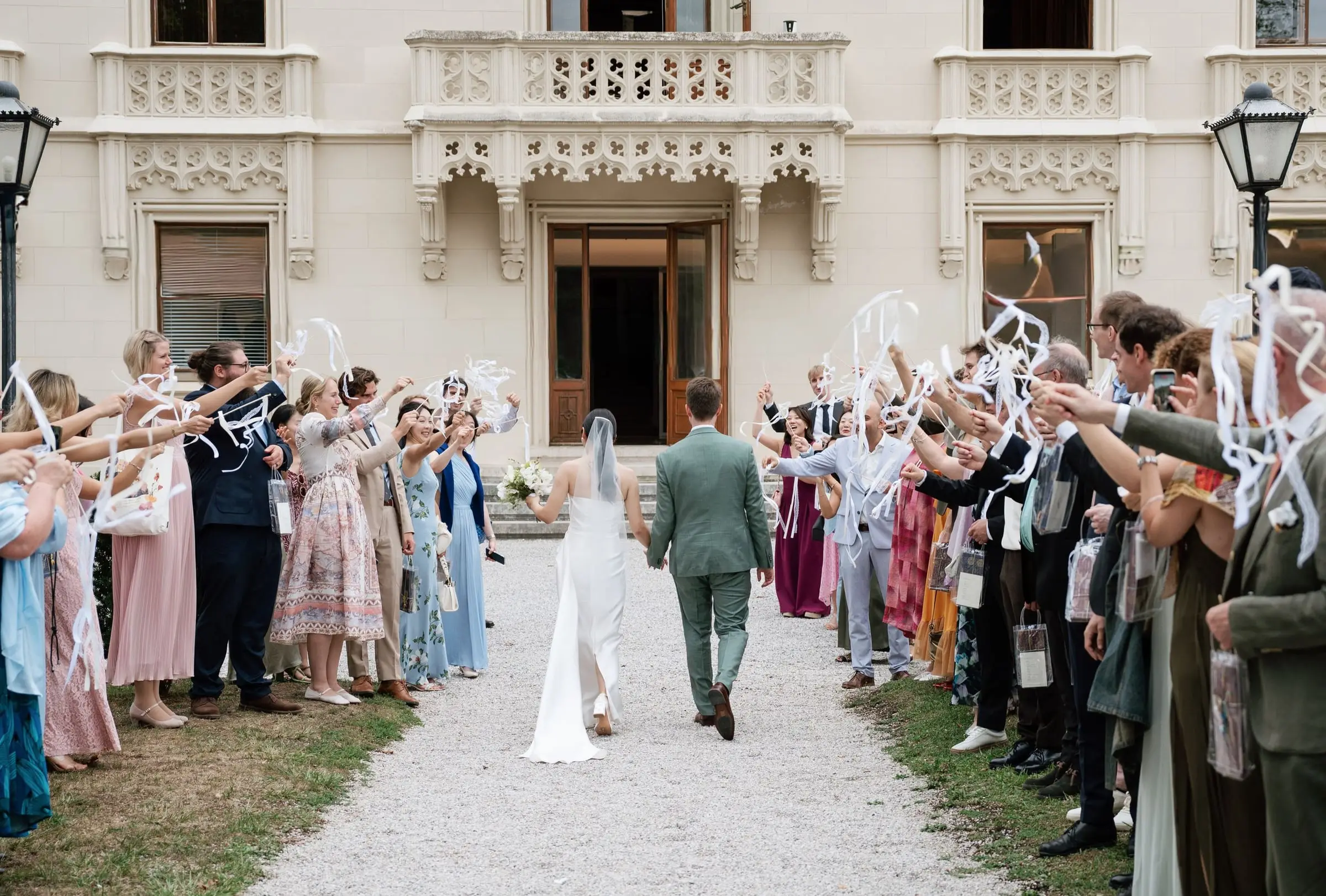 Newlyweds walking through guests waving ribbon wands at the castle