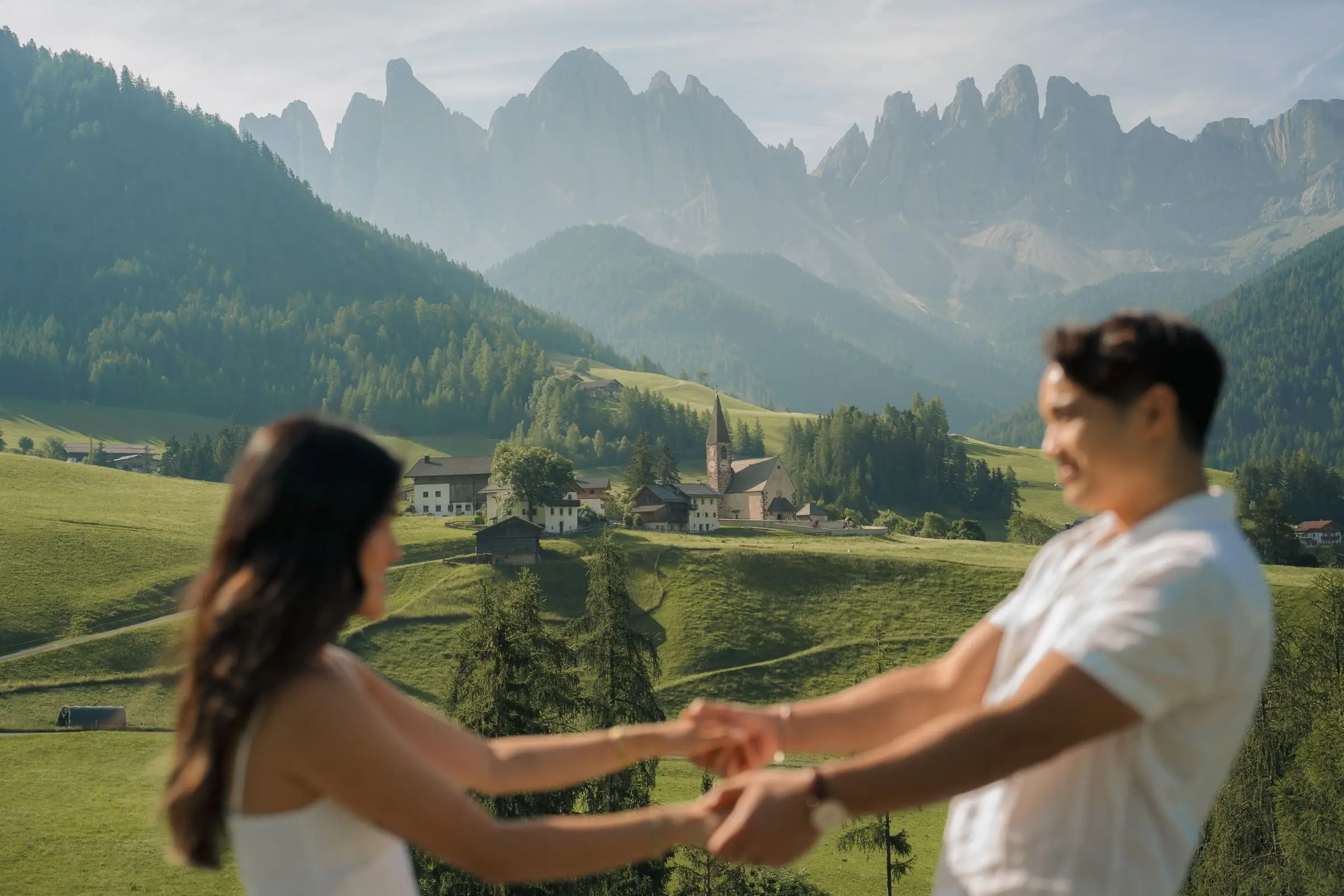 Couple holding hands above Santa Maddalena village and the Odle peaks