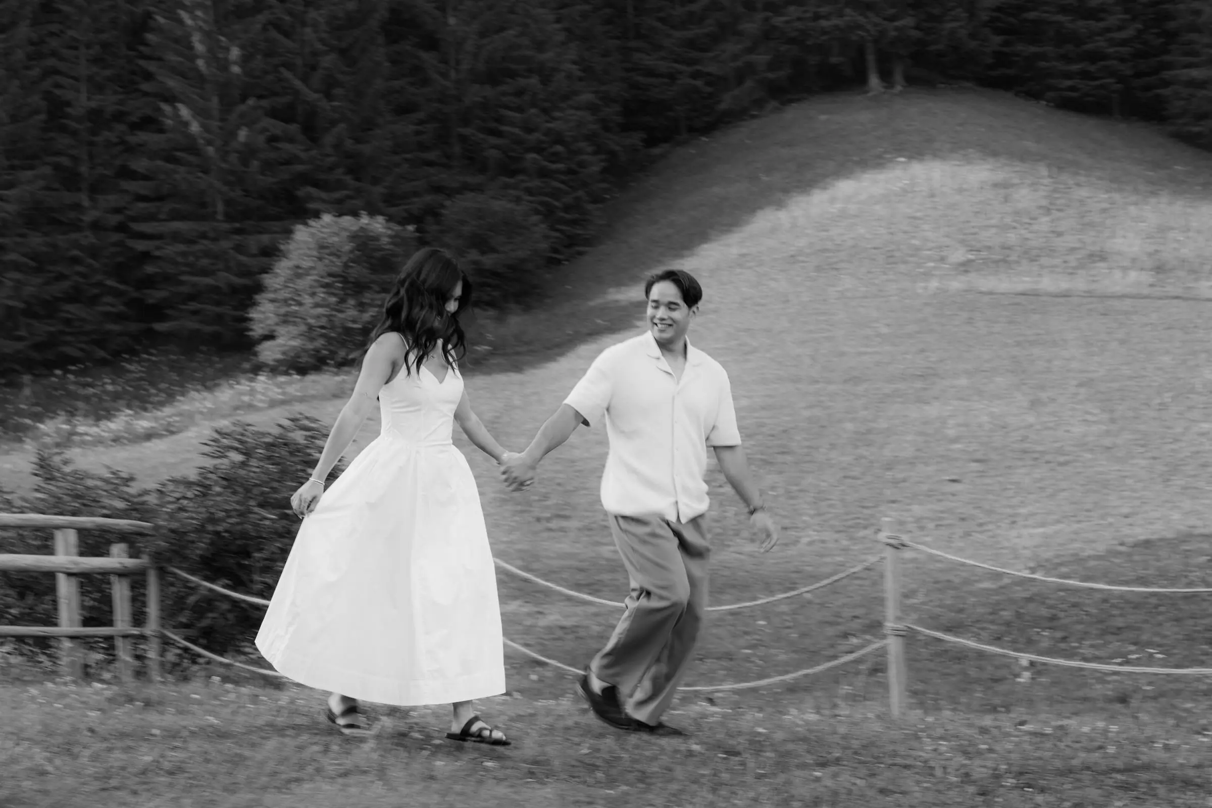 Black and white photo of the couple walking hand in hand along a fence
