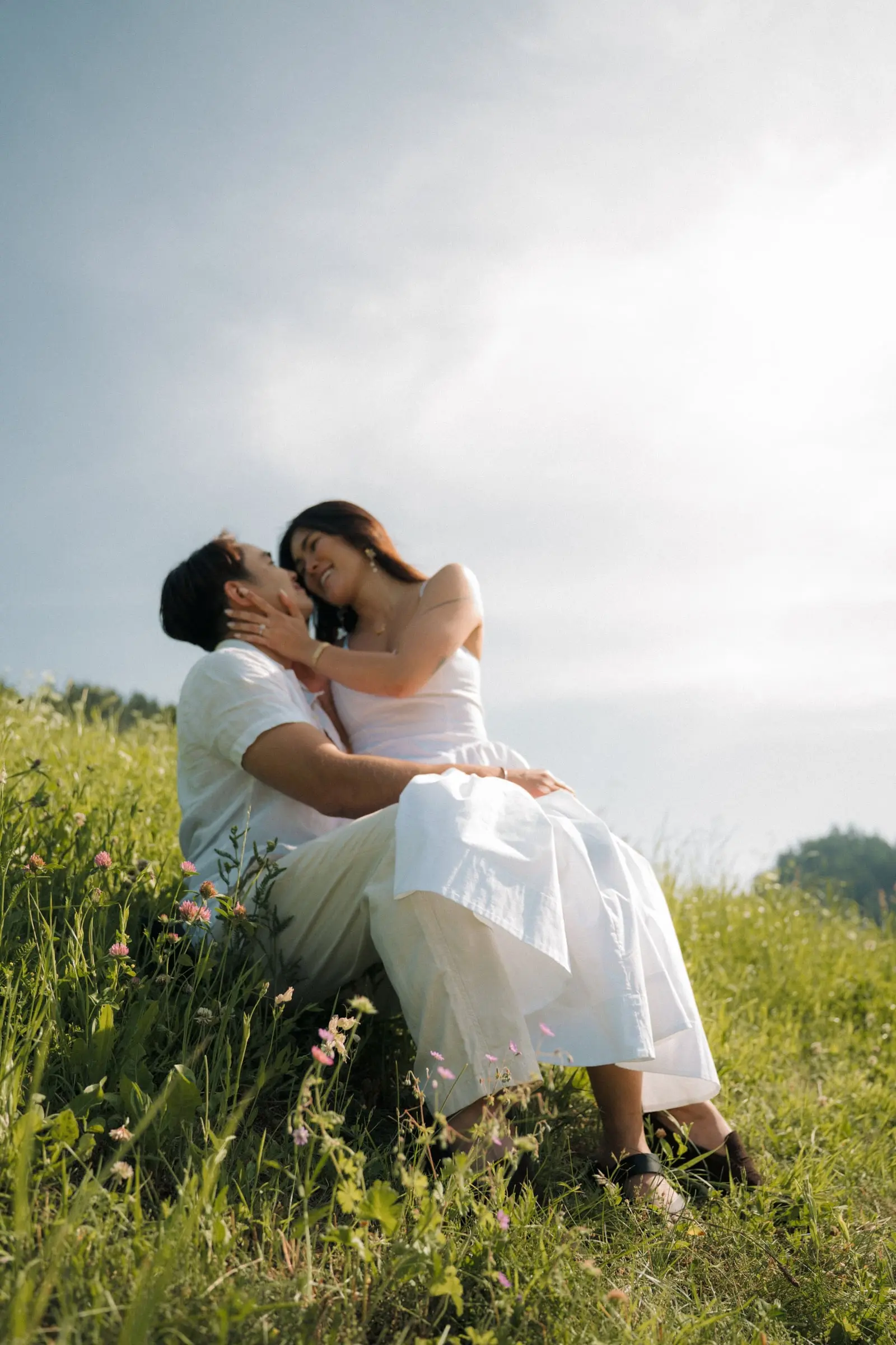 She sits on his lap in the tall grass, both smiling