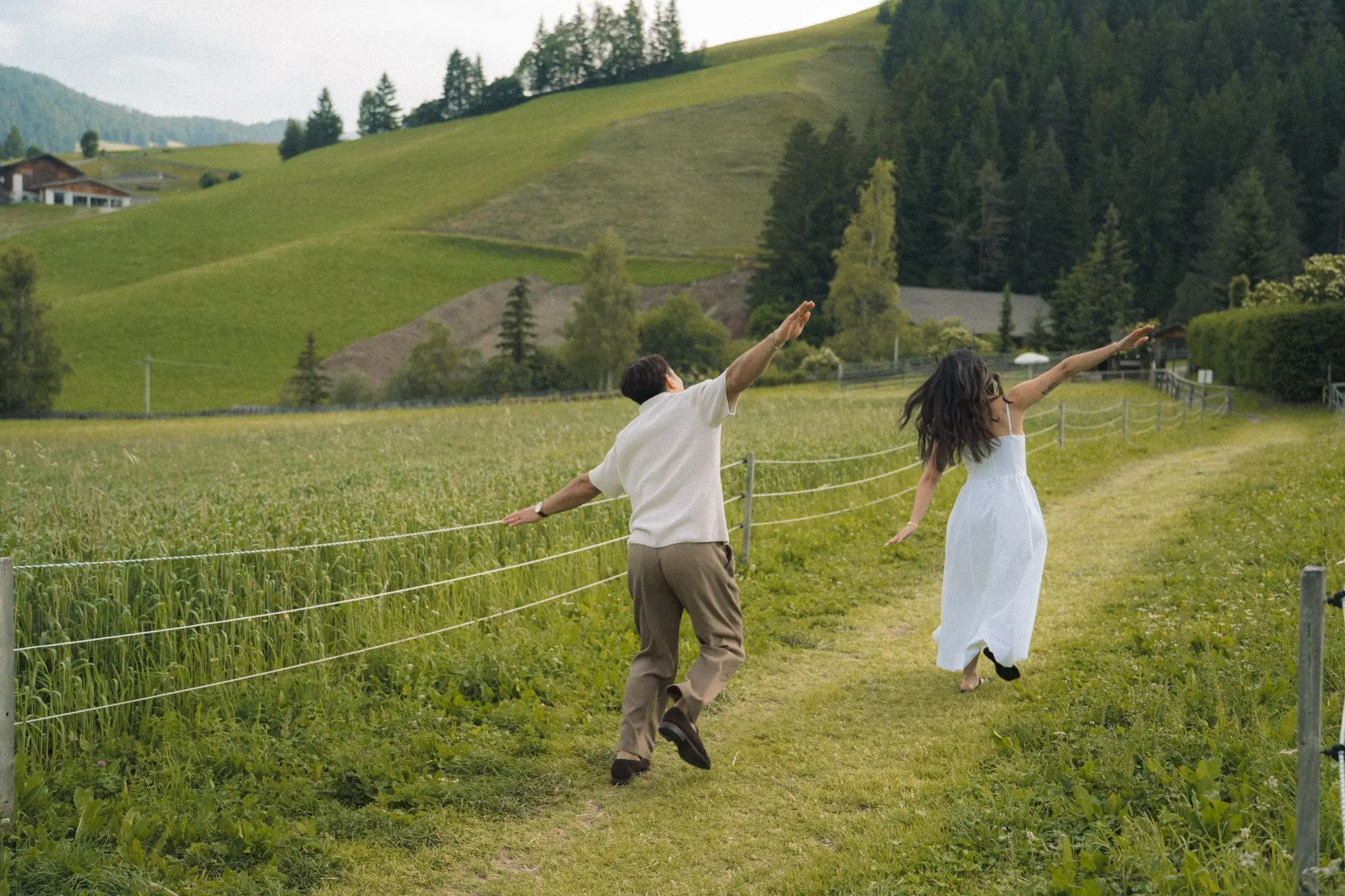 Couple running playfully with arms spread along a meadow path