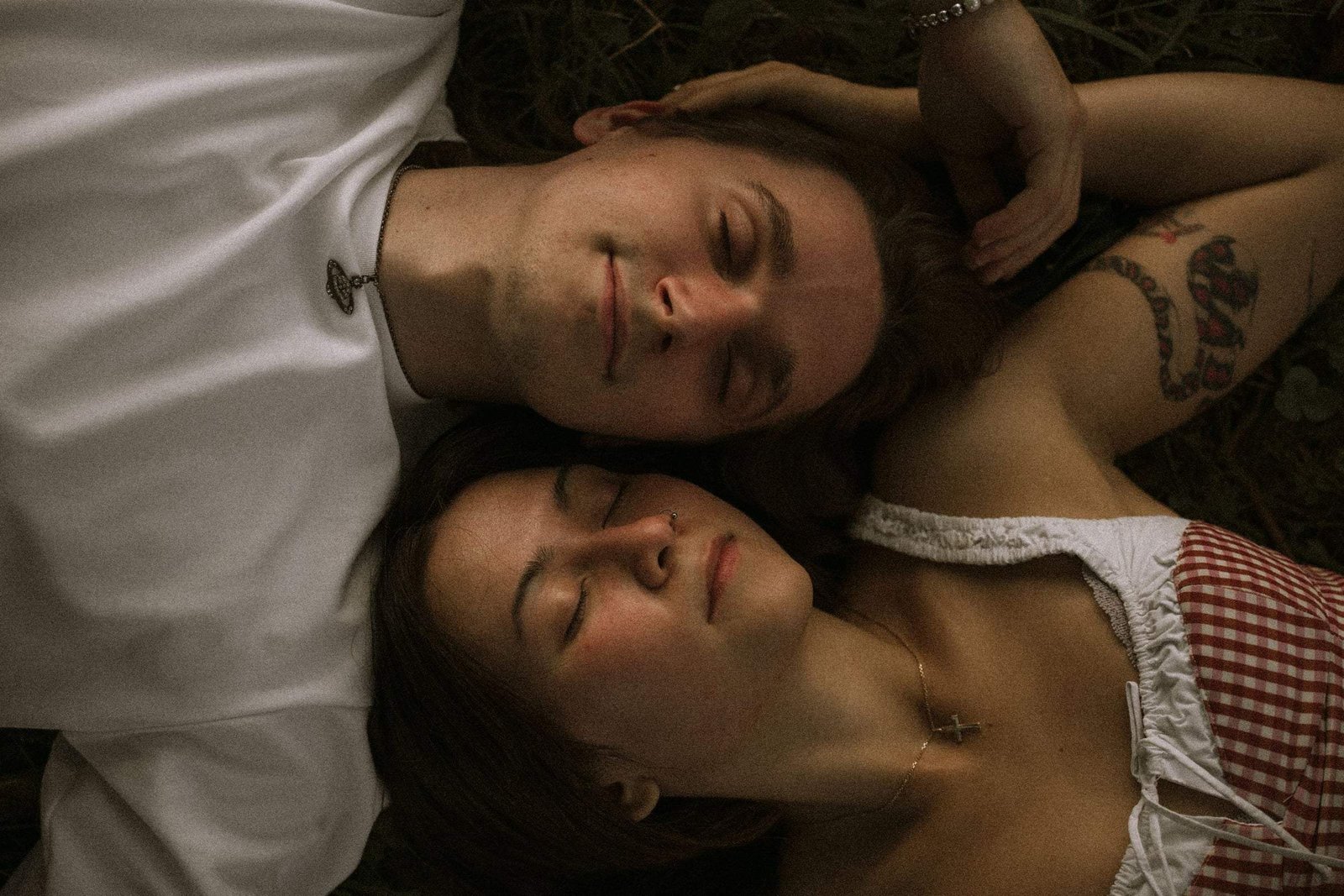 Couple lying in the grass, heads together, eyes closed